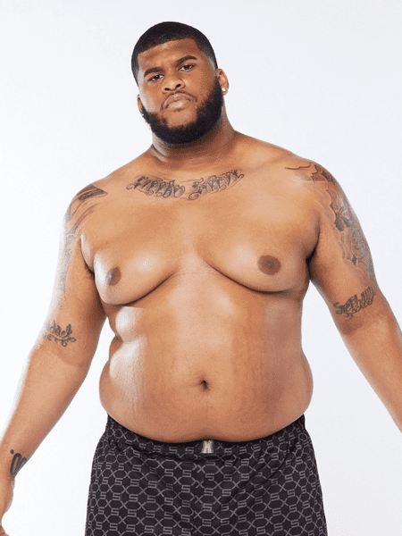 Modelo da fenty, um homem negro, gordo, com estrias na barriga, tatuagem no colo e nos braços, de barba e usando uma cueca da grife.