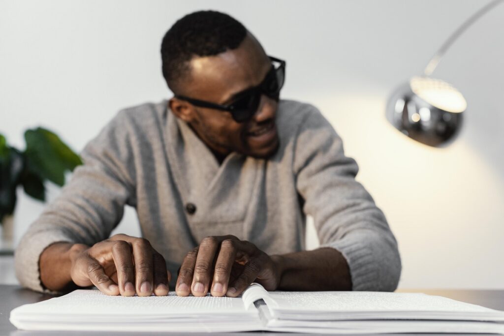 Homem com deficiência visual lendo livro em Braille enquanto sorri.