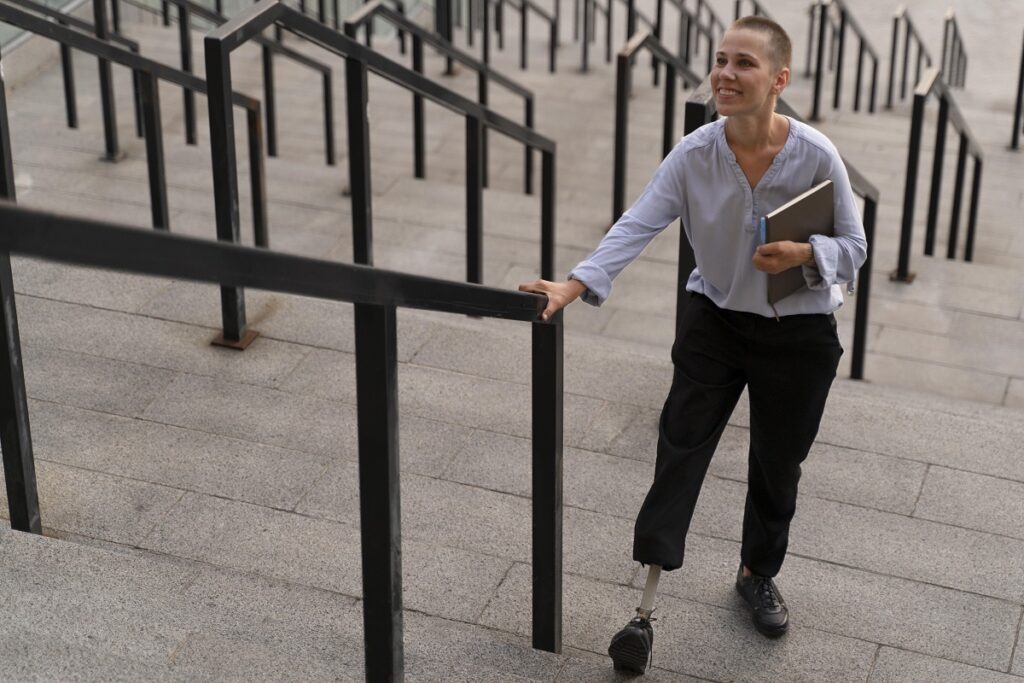 Mulher com deficiência sorri enquanto sobre escada em local sem rampa para acessibilidade.