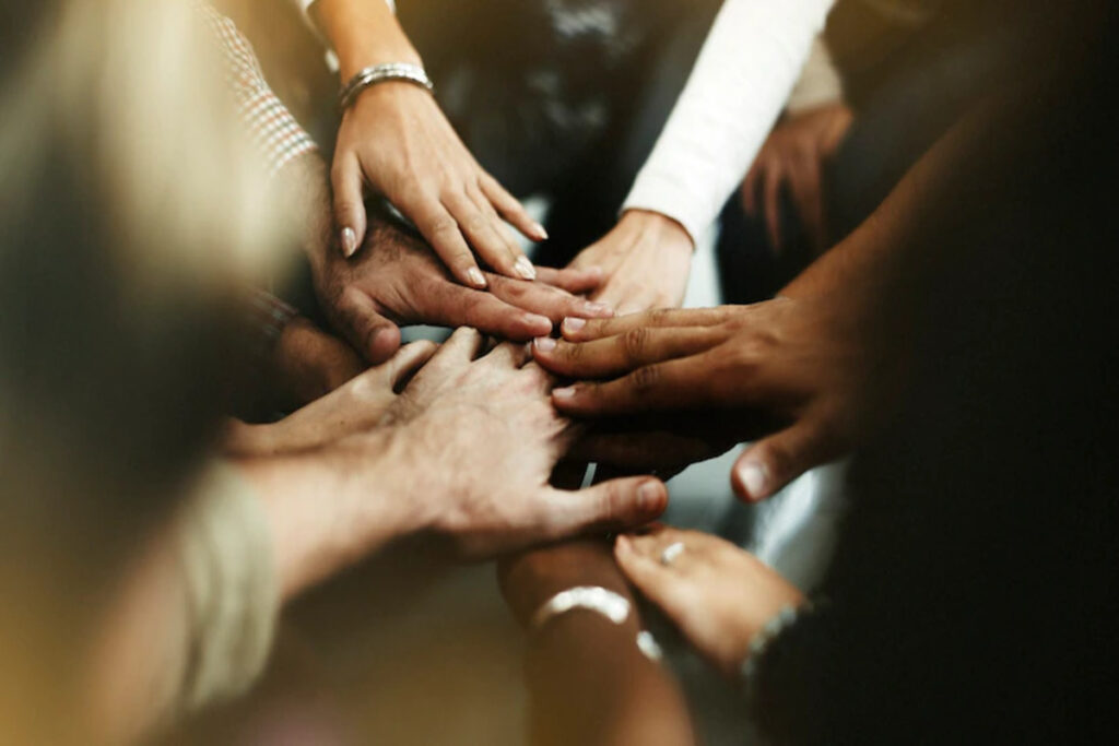Imagem de colaboradores de diversas etnias de empresa com RH inclusivo dão as mãos como um time.