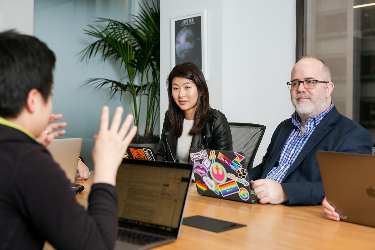 mulher asiática e homem de meia idade sentados em uma mesa de reunião com outros colegas