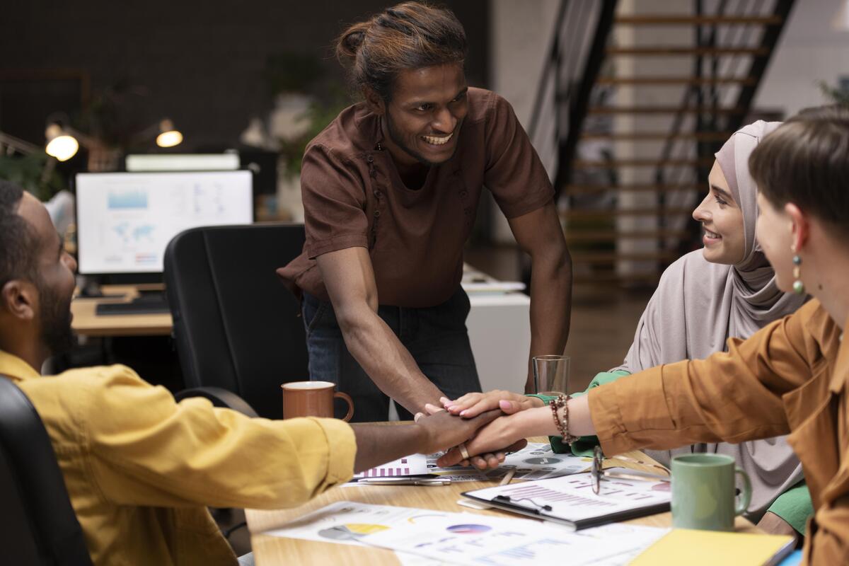 Imagem de uma equipe juntando a mãos no centro de uma mesa como um time