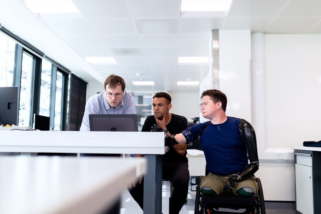 homem de cadeira de rodas, junto com dois colegas em uma mesa de reunião