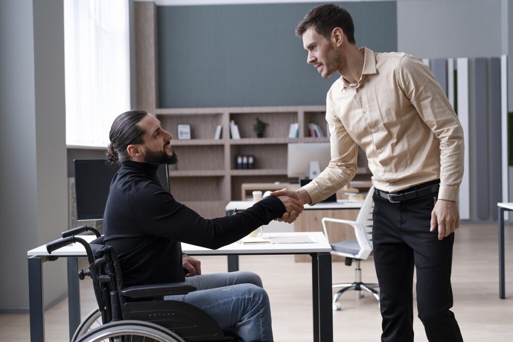 Benefícios inclusivos: A imagem mostra dois homem, sendo um cadeirante, apertando as mãos. 