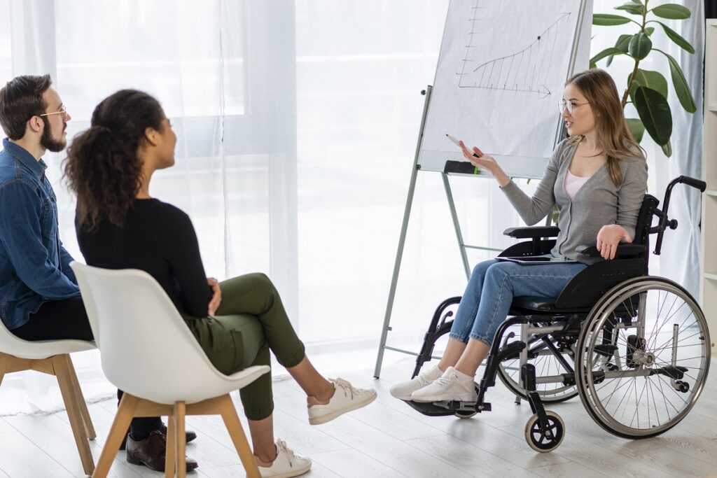 Gestão da diversidade e inclusão: A imagem apresenta uma mulher cadeirante explicando um assuntos para um homem e para outra mulher. 