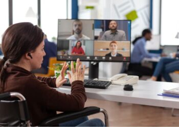 Mulher cadeirante em local de trabalho participando de reunião online com outras pessoas em seu computador