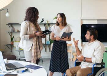 Homem em cadeira de rodas com duas mulheres em conversa em local de trabalho