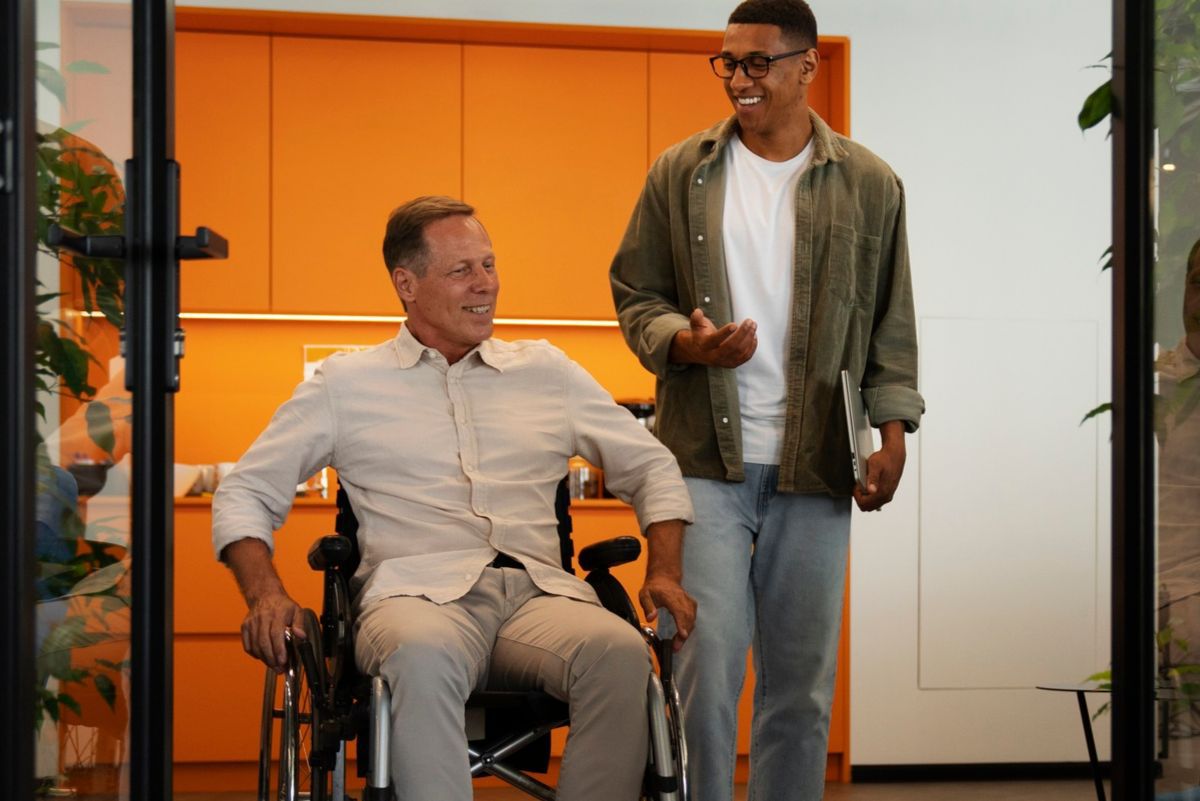 Homem em cadeira de rodas ao lado de colega em corredor conversando em local com cultura inclusiva
