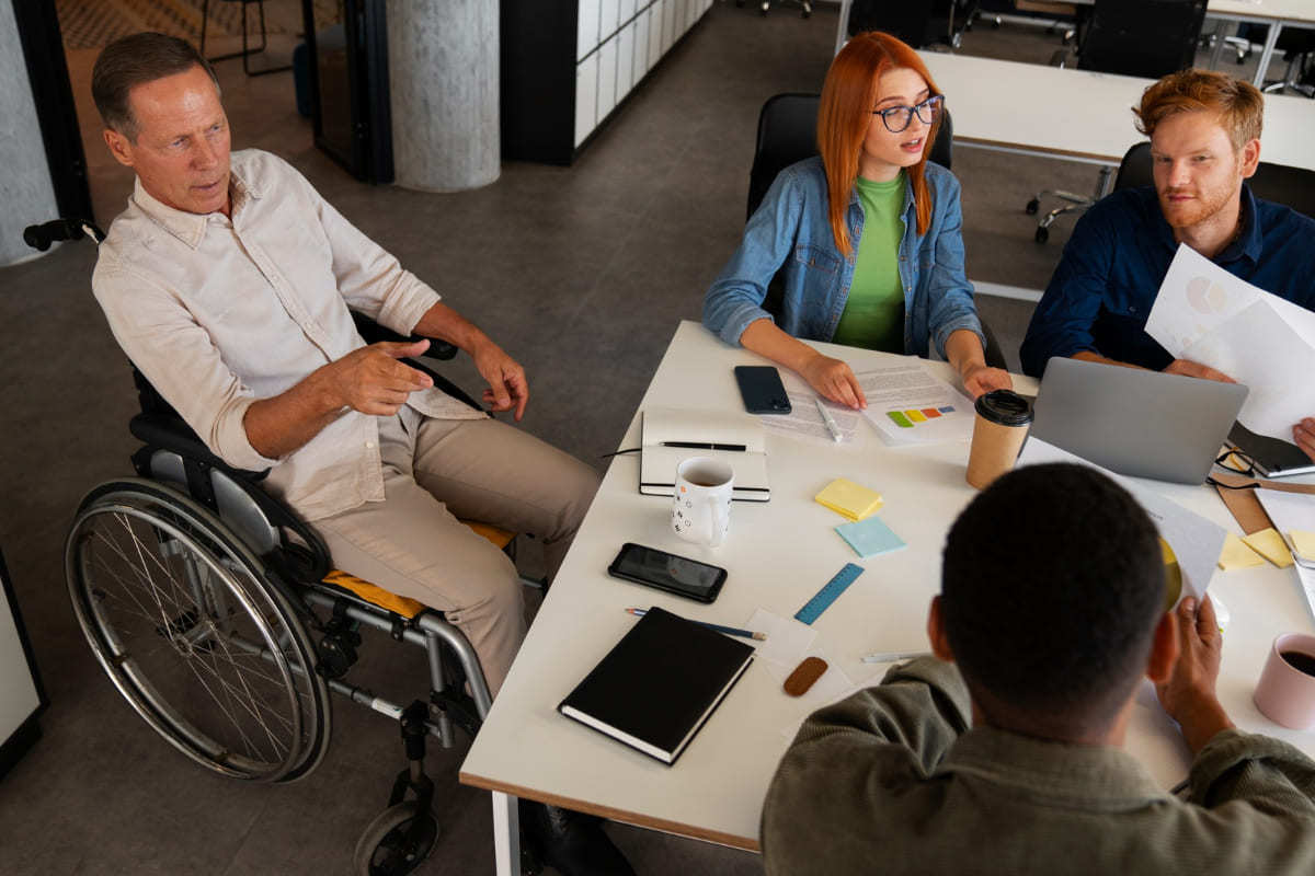 Homem em cadeira de rodas conversando com pessoas de diversas etnias em empresa que pratica Exemplo de inclusão