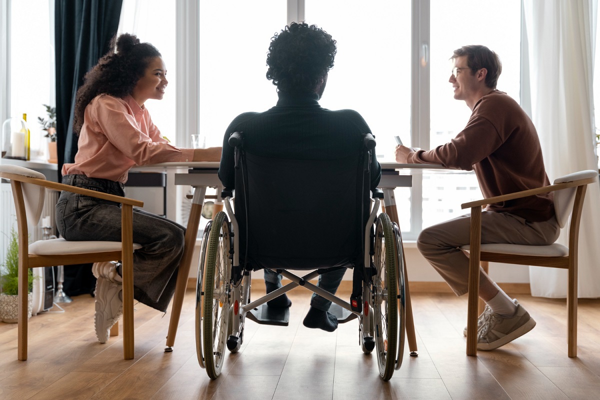 Local de trabalho com Plano de inclusão com homem cadeirante conversando com homem e mulher ao redor de mesa