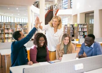 Homens e mulheres em local de trabalho se olhando sorridentes e tocando as palmas das mãos em comemoração
