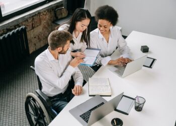 Homem em cadeira de rodas conversando com duas mulheres em escritório com empresa que pratica a Retenção de talentos