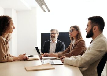 Mulher sentada diante de dois homens e outra mulher em local de trabalho