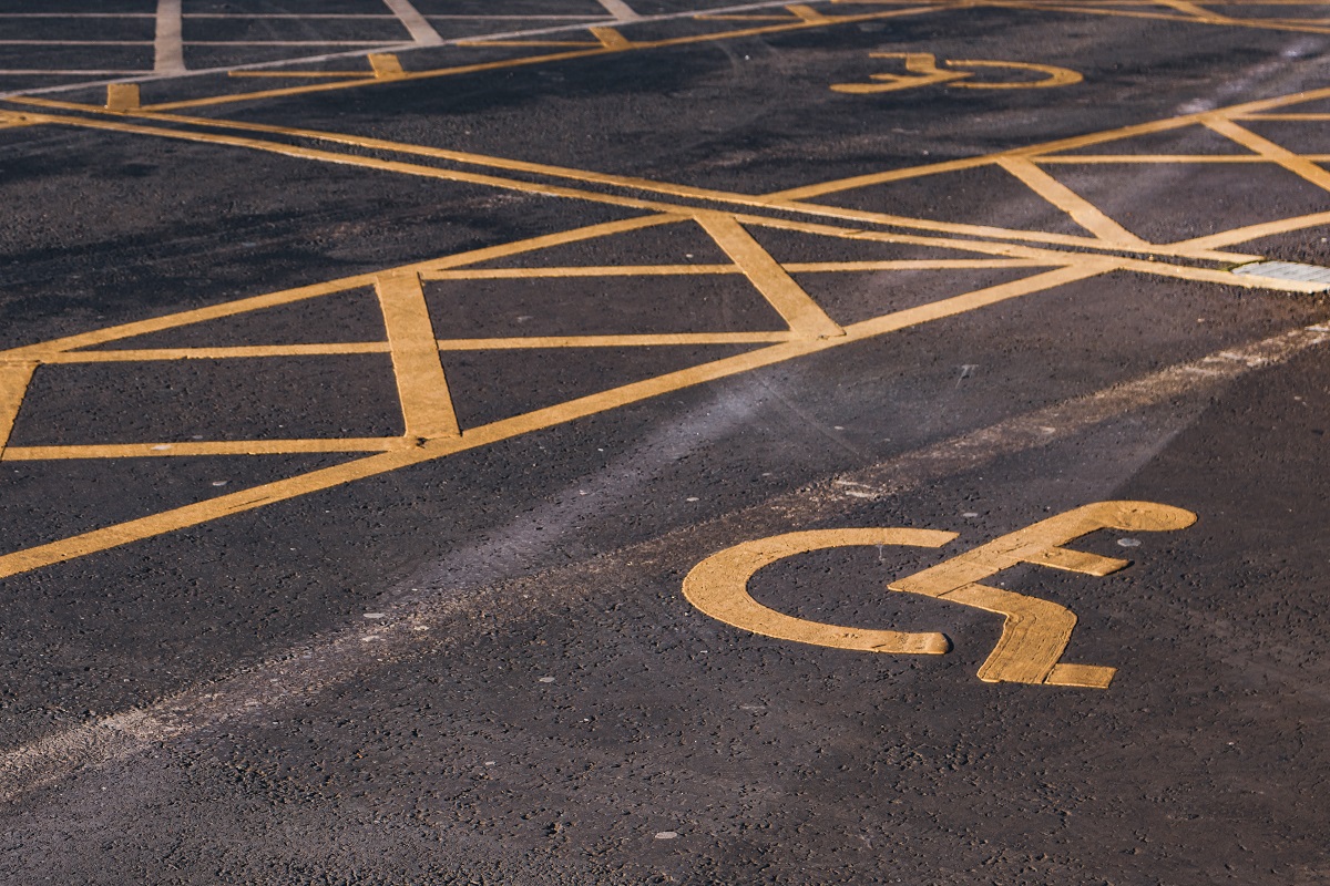 Estacionamento com marcações no chão em amarelo delimitando vagas para locais que fazem a Contratação de pessoa com deficiência com símbolo de acessibilidade no centro desses espaços