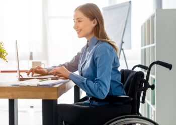 Mulher em cadeira de rodas diante de mesa de madeira em escritório de empresa com cultura diversa