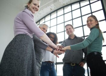 Funcionários inclusivos dão as mãos em círculo em local de trabalho enquanto sorriem e posam para foto