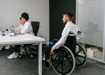 imagem ilustra duas pessoas em um escritório, indicando o porquê de empregar pessoas com deficência, já que uma das pessoas é um cadeirante