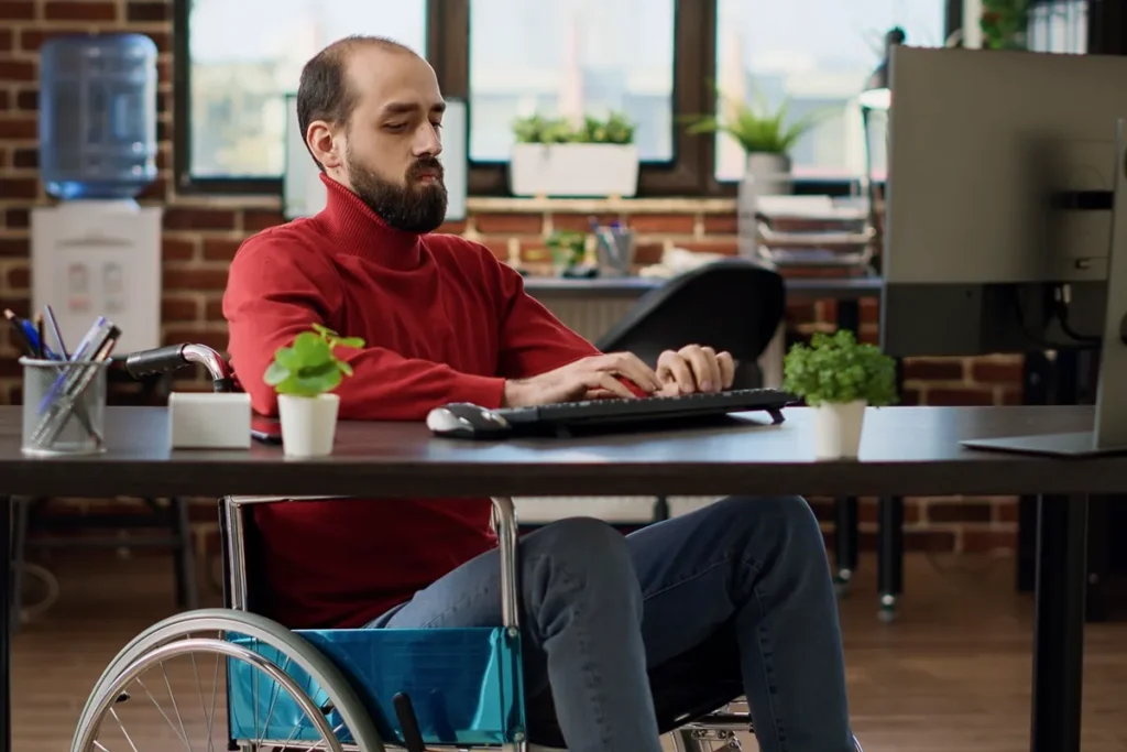 Homem cadeirante trabalhando em um escritório moderno, demonstrando inclusão no ambiente corporativo e acessibilidade no local de trabalho.