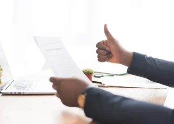 Mão de um profissional segurando um documento enquanto faz um sinal de positivo, indicando aprovação no processo de contratação.