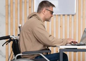 Homem utilizando um laptop em cadeira de rodas, destacando a inclusão no aprendizado online.
