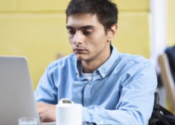 Homem jovem com expressão concentrada estudando online em um laptop, simbolizando o aprendizado digital e o e-learning.
