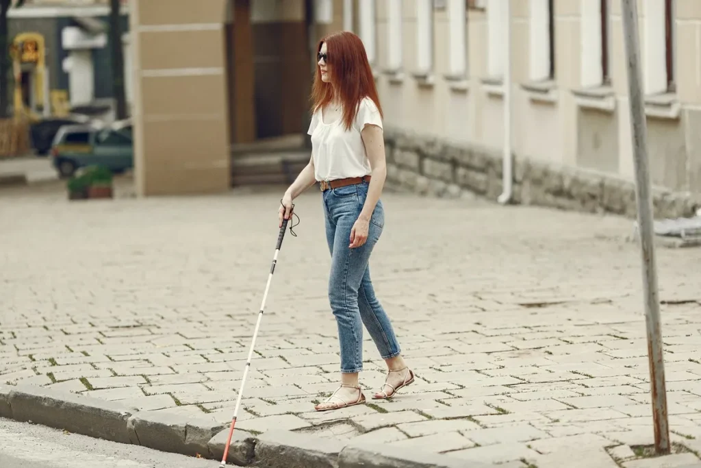 Mulher com deficiência visual caminhando em uma calçada com o auxílio de um bastão de orientação.