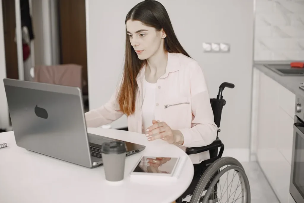 Mulher em cadeira de rodas usando um laptop em um ambiente de home office, com foco no trabalho.