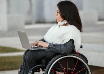 Mulher em cadeira de rodas usando um laptop ao ar livre, representando acessibilidade e inclusão no trabalho remoto.