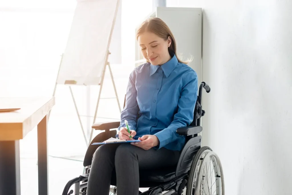 Mulher em cadeira de rodas usando um uniforme azul, preenchendo um formulário em uma prancheta no ambiente de um escritório iluminado.