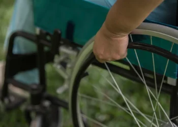 Close-up de uma mão movimentando a roda de uma cadeira de rodas azul, em um ambiente ao ar livre com grama verde.