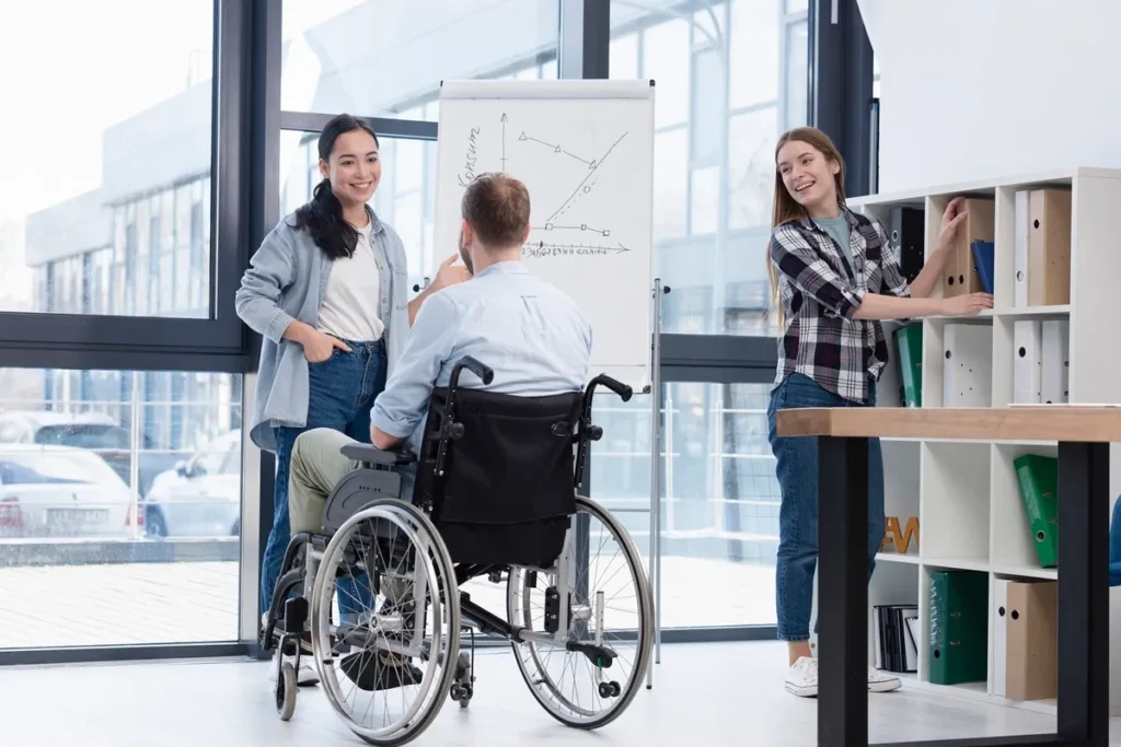 Equipe diversa em ambiente de trabalho colaborativo, com um profissional cadeirante participando de uma apresentação diante de um quadro branco.