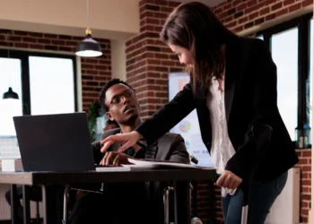 Mulher com deficiência usando muletas e colaborando com colega cadeirante em ambiente corporativo moderno