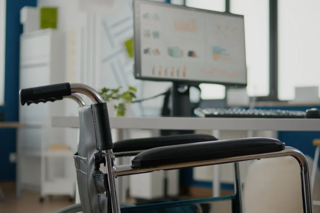 Cadeira de rodas posicionada ao lado de mesa com computador em escritório moderno e acessível