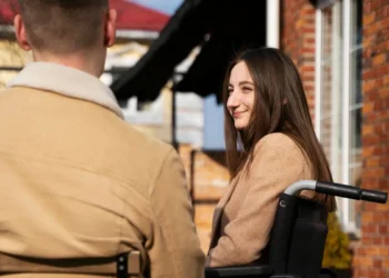 Mulher jovem em cadeira de rodas sorri enquanto conversa com um homem ao ar livre, simbolizando rede de apoio emocional