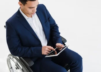 Homem cadeirante vestido com terno azul e camisa branca usando um tablet, simbolizando inclusão e acessibilidade no ambiente de trabalho.