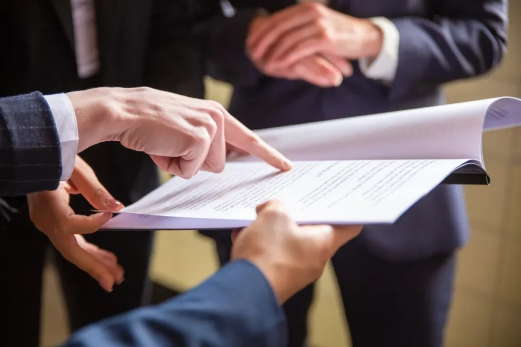 Imagem de mãos discutindo um contrato ou documento jurídico durante uma reunião, com uma pessoa apontando para o texto